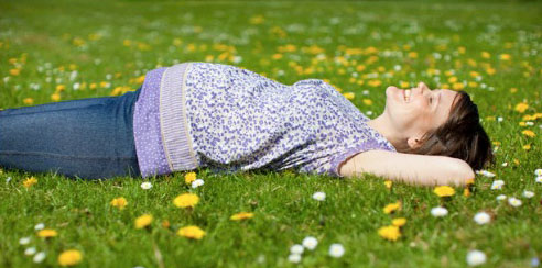 Mujer embarazada en el pasto con flores