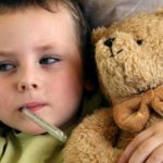 Niño en cama con termómetro junto a un osito de peluche