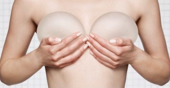 Mujer sosteniendo implantes mamarios sobre su pecho