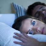 Mujer joven con insomnio en la cama con marido
