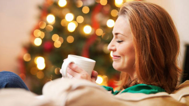 Mujer relajada tomando una taza caliente junto a un árbol de navidad, fin de año