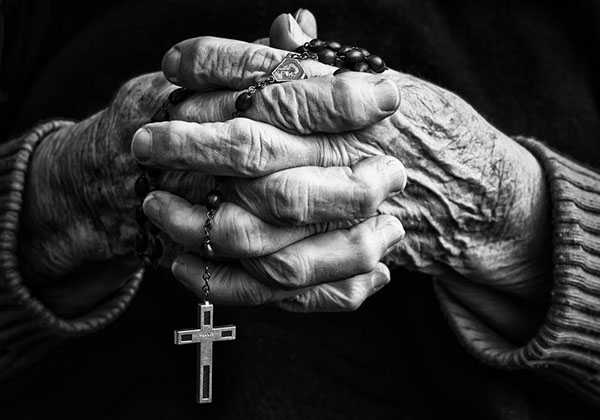 Manos arrugadas de anciano con rosario cruz