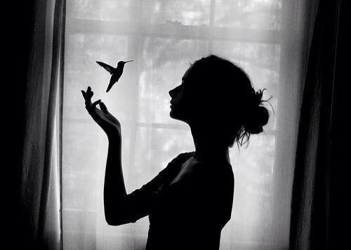 Mujer pensando en la ventana con un colibrí